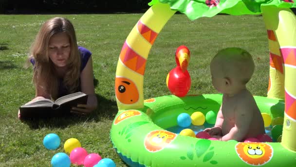 Mia madre ha letto un libro sul plaid e il bambino nella piscina per bambini. 4K — Video Stock