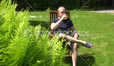 Gün ortasında tahta sandalyede oturan alkolik adam içki bira. 4k
