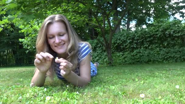 Crazy woman pull petals from daisy flower bloom laying on grass. 4K — Stock Video