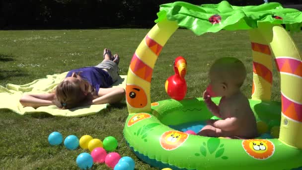 Careless mother lay on plaid and baby splash water in kiddie pool. 4K — Stock Video