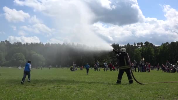 Brandman med slang spray vatten under glada barn barn i parken. 4K — Stockvideo