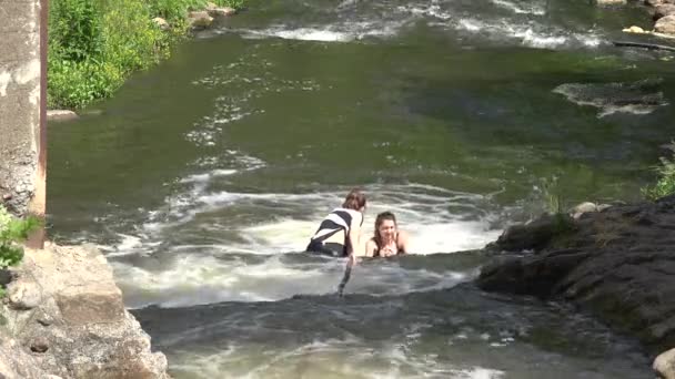 Mujeres jóvenes vadean para superar la cascada de ríos de agua salvaje. 4K — Vídeo de stock