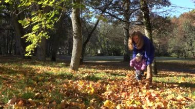 park kaplı sonbahar yaprakları küçük çocuk ile anne oynamak. 4k