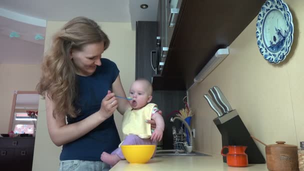 Mãe descuidada mulher alimentar bebê na mesa na cozinha. 4K — Vídeo de Stock