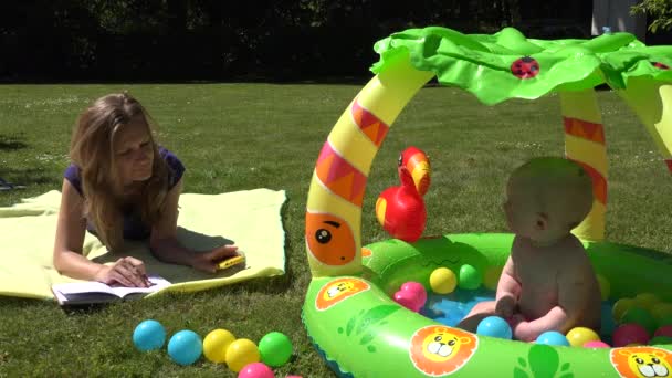 Femme d'affaires avec smartphone sur carreaux et bébé triste dans la piscine pour enfants. 4K — Video