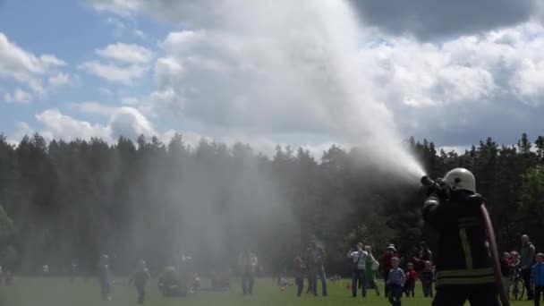 Pompiere spruzzare acqua dal tubo e bambini corrono sotto gocce d'acqua. 4K — Video Stock