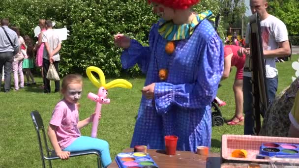 Clown schilderen met kleuren op meisje gezicht in groen park. 4k — Stockvideo