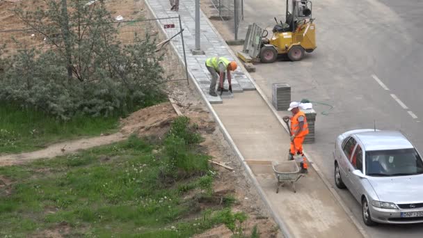 Lavoratori carico di sabbia in carriola e pavimentare laici piastrelle. 4K — Video Stock