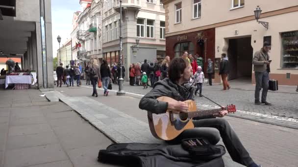 Dospělý muž si hraje s ústní vodou a kytarou a lidi chodí pěšky. 4k — Stock video