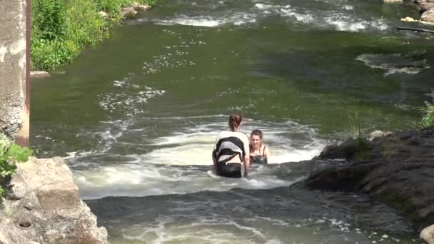 Zwei junge Mädchen waten, um die Wildwasserkaskade zu überwinden. 4k — Stockvideo