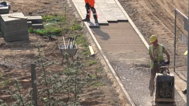 Arbetaren låg kakel och tryck spillrorna med plattan komprimator på trottoaren. 4K — Stockvideo