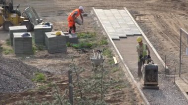 İşçiler plaka sıkıştırıcı ile molozlara basınç uygular ve kaldırıma fayanslar serer. 4K