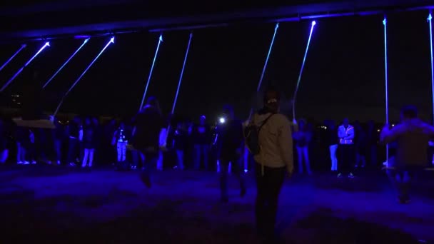 Люди ждут в ряд и катаются на веревках качели на неоновом свете ночью. 4K — стоковое видео