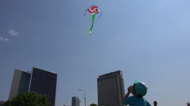 Young boy flies his kite high in sky between skyscraper in city center. 4K — 图库视频影像