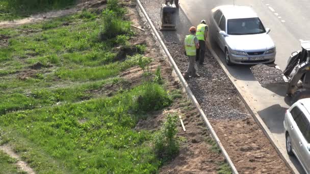 トラクターは瓦礫を降ろし、労働者は道路の近くでそれを平準化します。4k — ストック動画