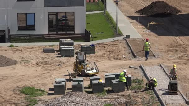 Arbetare gör kakel trottoar trottoar nära nya platt hus. 4K — Stockvideo