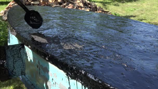 Les mains du réparateur versent du goudron chaud sur le fond du bateau en bois. 4K — Video