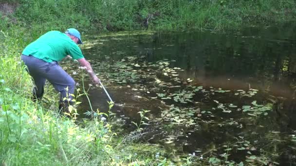 与从草镰刀工具清洁池塘的鱼育种农场工人。4 k — 图库视频影像