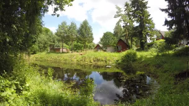 Pueblo alberga edificios cerca de lago estanque y las nubes flotan en el cielo azul. 4K — Vídeos de Stock