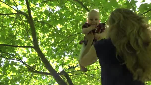 Молодая мама поднимает свою счастливую дочку под тюльпановое дерево в парке. 4K — стоковое видео