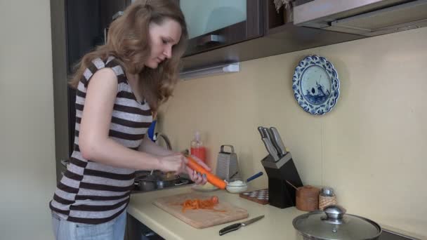 主婦の女性はピーラーツールでオレンジニンジンを皮をむきます。4k — ストック動画