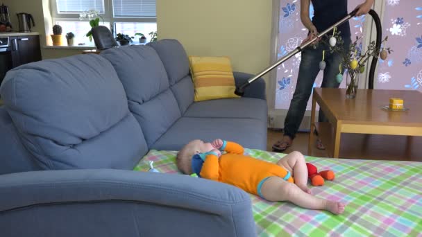 Madre sofá limpio con aspiradora y pequeño bebé jugar cerca. 4K — Vídeos de Stock