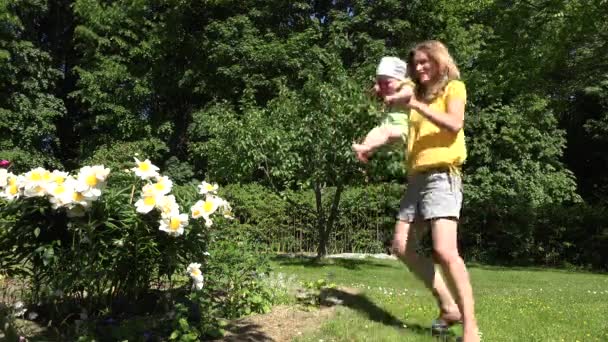 Счастливая мама с малышкой разворачиваются в саду рядом с пионскими цветами. 4K — стоковое видео