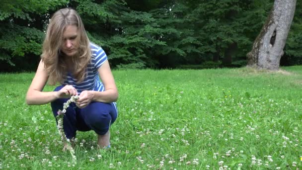 Leuk meisje in blauwe geweven hoofd kroon van Klaver plant bloeit. 4k — Stockvideo