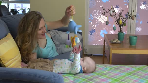 Kvinnan en nyfiken baby dotter spela med leksak på soffan. 4k — Stockvideo