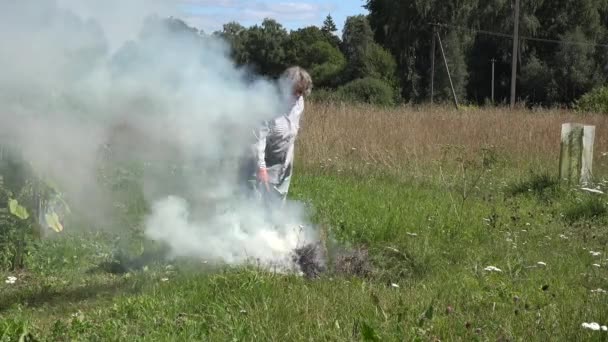 A mulher sênior queima grama e recusa-se no fogo no prado no quintal de aldeia rural. 4K — Vídeo de Stock