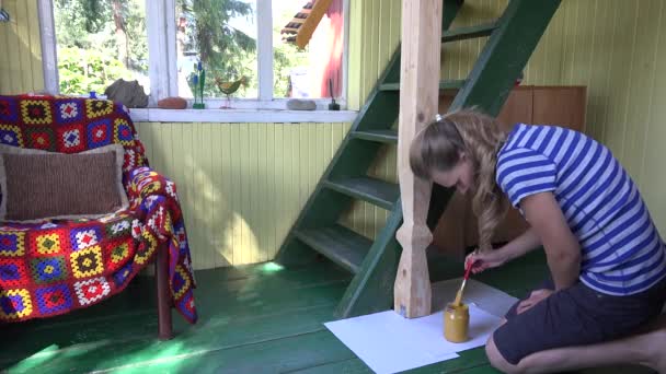 Mulher loira pintando poste de coluna de madeira com pincel de cor amarela no quarto acolhedor rural. 4K — Vídeo de Stock