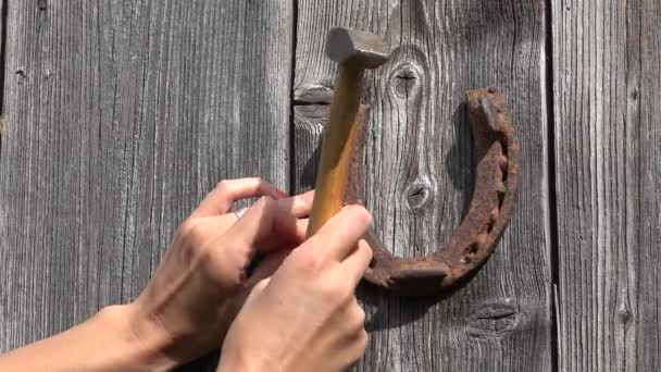 Mano femenina clavos de martilleo y colgar caballo oxidado zapato símbolo de la suerte en la puerta de la casa del jardín. 4K — Vídeo de stock