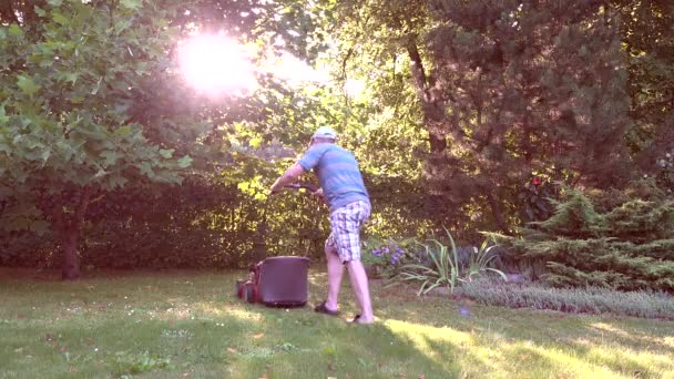 Homme couper l'herbe avec tondeuse à gazon dans le jardin au coucher du soleil en soirée. 4K — Video