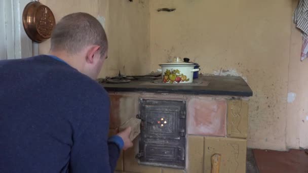 O aldeão pôs lenha no fogão da cozinha rural. 4K — Vídeo de Stock