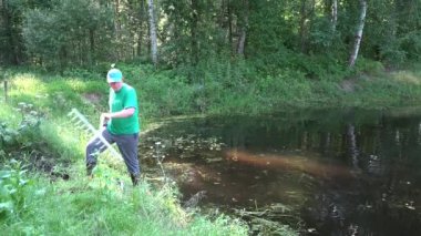 Tırmık aleti ile Bahçıvan adam çim ve çamur dan gölet suyu temizler. 4k