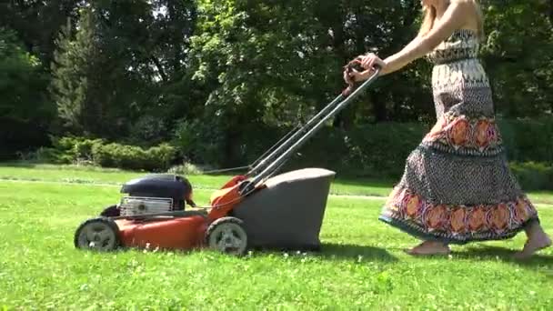 Mujer en vestido largo cortar hierba en su propio patio con cortacésped. 4K — Vídeo de stock