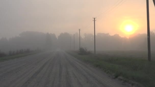 Carro conduzir estrada de cascalho rural em densa neblina. Nascer do sol enevoado na manhã de outono. 4K — Vídeo de Stock