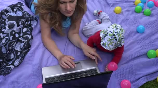 Bébé enfant interrompre mère travailler avec ordinateur sur plaid dans le jardin. 4K — Video