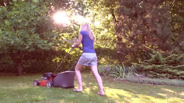 Femme ouvrière blonde tondre l'herbe pendant la belle lumière du soleil du soir dans la cour. 4K — Video