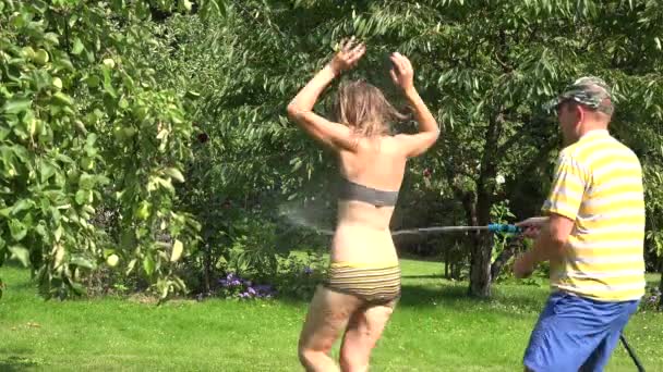 Mann wässert Frau im Badeanzug mit Wasserschlauch grün Park. 4k — Stockvideo