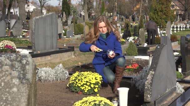 Kvinnan tänder ett ljus på fars grav på kyrkogården. 4K — Stockvideo