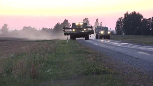Traktor s přívěsem převíjí těžký skliďový stroj na venkovské silnici při západu slunce. 4k — Stock video