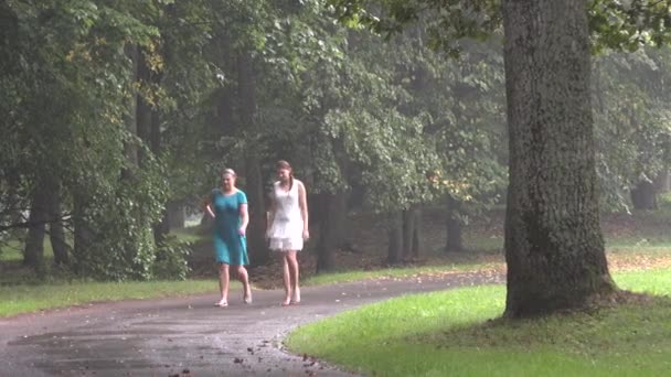 Dos mujeres jóvenes caminan en el parque verde temprano en la mañana después de la lluvia. 4K — Vídeos de Stock