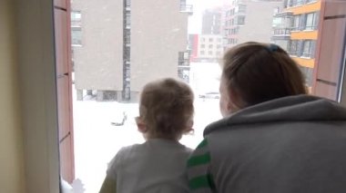 Anne ve bebek düz evin odasında penceresinden görünümlü düşen kar keyfini çıkarın. 4k