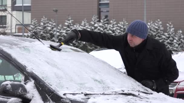 Человек со скребком царапает снег и лед из окна машины зимой. 4K — стоковое видео