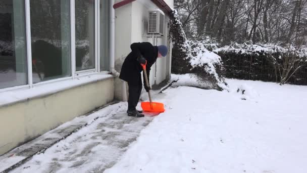 Worker shoveling snow from sidewalk in front of his house after snowfall. 4K — Stock Video