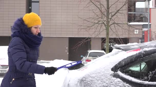 Женщина убирает снег из машины щеткой в жилом доме районного двора. 4K — стоковое видео