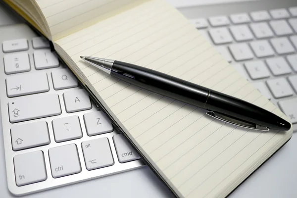 Bloc de notas y pluma en un teclado de computadora — Foto de Stock