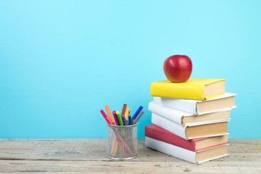 Kitaplar istifleniyor. Kitaplar ahşap masada ve mavi arka planda. Okula dönelim. Reklam metni için alanı kopyala