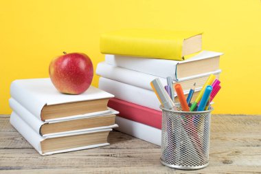 Kitaplar istifleniyor. Tahta masadaki kitaplar ve sarı arka plan. Okula dönelim. Reklam metni için alanı kopyala